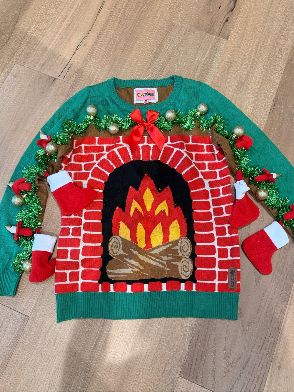 Tipsy Elves Green Sweater with Red Brick Fireplace and Gold Accents